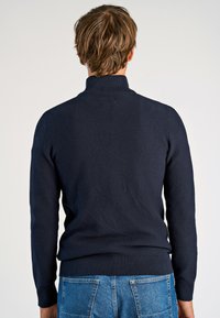 Marineblauer Strickpullover mit hohem Kragen, strukturiertem Muster und geripptem Saum. Tragen Sie ihn mit blauen Jeans, die einen lässigen Stil zeigen.
