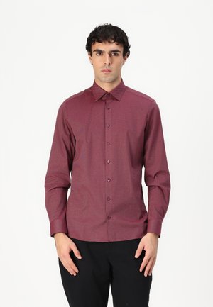 Chemise à manches longues, boutonnée, de couleur rouge foncé avec un motif texturé. Présente un col classique et des boutons à l'avant, associée à un pantalon sombre.