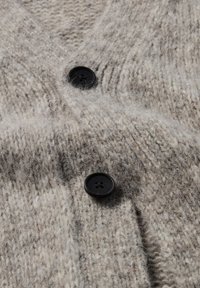 Beige gebreide cardigan met een textuurpatroon, voorzien van twee zwarte knopen en een zachte, vlezige stofafwerking.