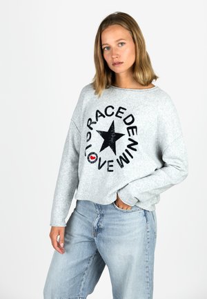 Hellgrauer, oversized Pullover mit einem schwarzen Stern und einem Textdesign in fetten Buchstaben. Aus weichem Fleecematerial mit angeschnittenen Schultern.
