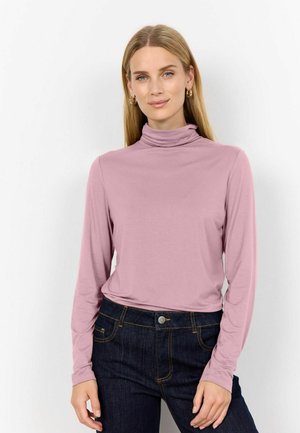 Lange mouwen, turtleneck top in lichtroze stof, gecombineerd met donkerblauwe jeans. Zachte textuur; passende stijl met een geraffineerde kraag.