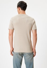 Beige ribbet kortærmet skjorte med rund hals, tætsiddende, parret med lyseblå denim jeans, der viser et afslappet, struktureret udseende.