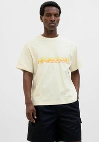 Crème-kleurig katoen T-shirt met korte mouwen en een ronde hals, met een geel grafisch logo op de voorkant.