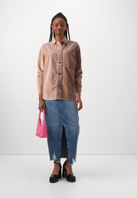Light brown corduroy button-up shirt with front pocket, paired with a distressed denim skirt featuring a front slit. Holds a pink handbag.