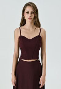 Top corto bordeaux con spalline sottili, scollatura a cuore e cuciture strutturate. Rifinito con un bottone decorativo sul lato.