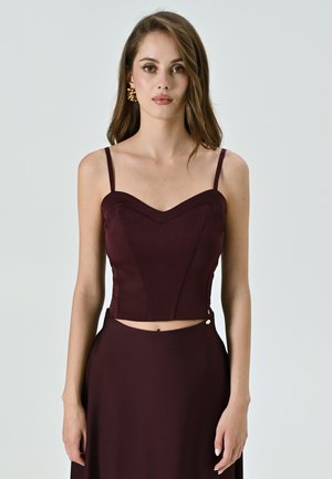 Top corto bordeaux con spalline sottili, scollatura a cuore e cuciture strutturate. Rifinito con un bottone decorativo sul lato.