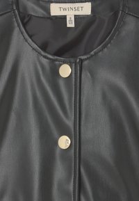 Giacca in ecopelle nera con colletto rotondo, dotata di tre bottoni a pressione metallici e texture liscia. Etichetta: Twinset, taglia 8.