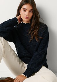 Tumes pitsi kudumisega sviiter kõrge krae ja soonikute otstega. Aktsenteerib kontrastne valge äär. Kanda heledate laia säärega pükstega.