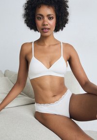 White soft-cup bra with thin straps, paired with white lace-trimmed panties. Smooth fabric texture, minimalist design.