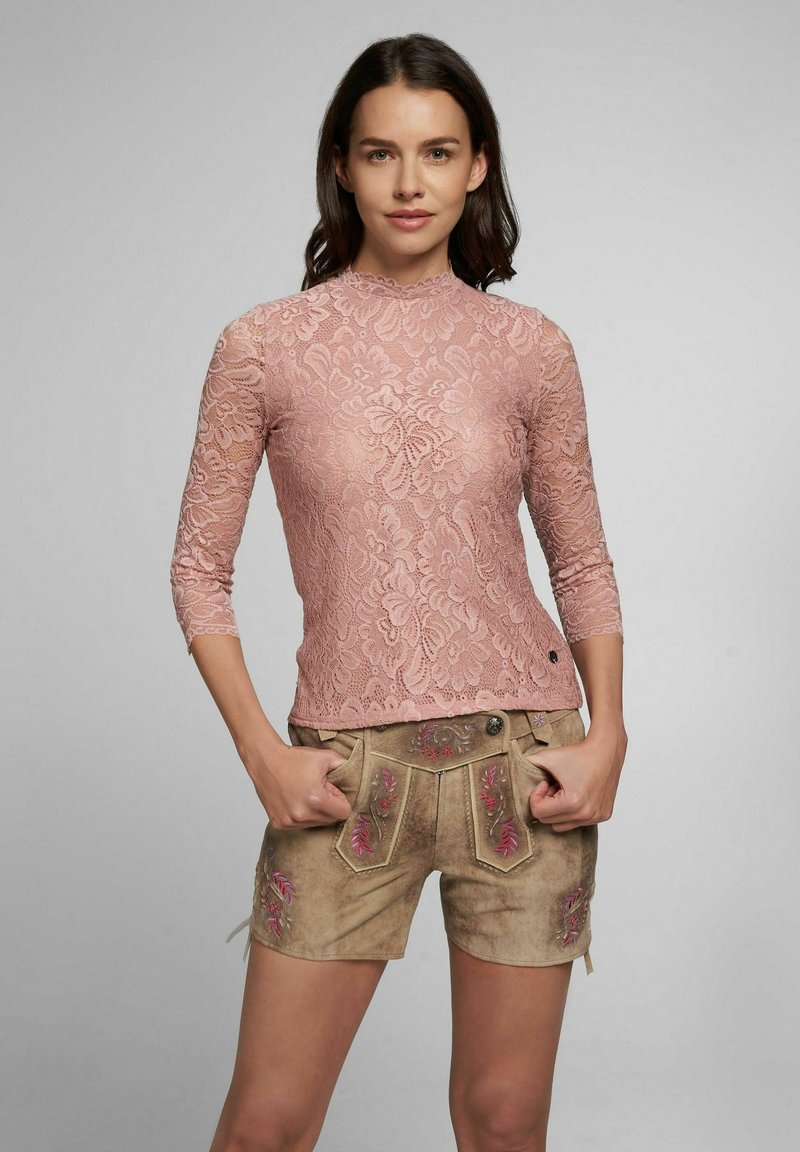 Rosa Spitzentop mit hohem Kragen und Dreiviertelärmel, kombiniert mit beigen Shorts mit floraler Stickerei und Taschen.