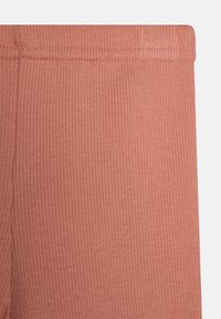 Ribbade stretchbyxor i en mjuk korallfärg, med en sömlös midja och slät textur, designade för komfort och flexibilitet.