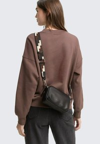 Felpa oversize marrone con una finitura morbida e testurizzata, abbinata a una borsa a tracolla in pelle nera con una tracolla decorata.