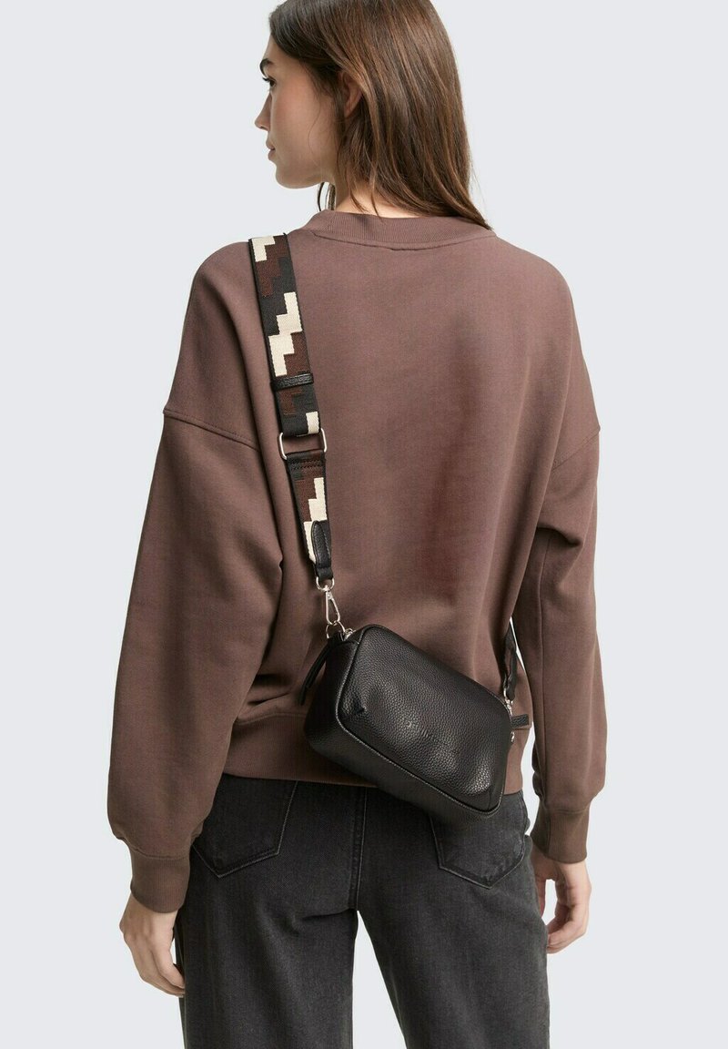 Felpa oversize marrone con una finitura morbida e testurizzata, abbinata a una borsa a tracolla in pelle nera con una tracolla decorata.