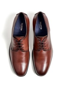 Braune Lederschuhe mit glatter Oberfläche, Schnürdesign, abgerundeter Zehenpartie und dezenten Nahtdetails. Schriftzug innen sichtbar.