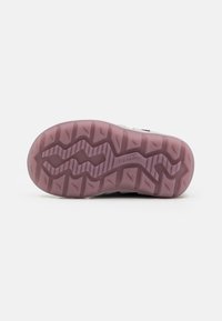 Semelle de chaussure avec une adhérence à motif ; matériau en caoutchouc rose avec des motifs en zigzag surélevés pour la traction ; texture lisse à la surface.