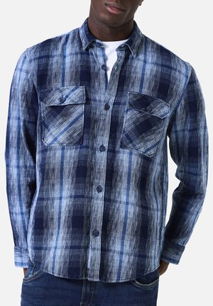 Chemise en flanelle avec un motif à carreaux bleu et blanc, manches longues, deux poches poitrine, devant à boutons et tissu texturé.