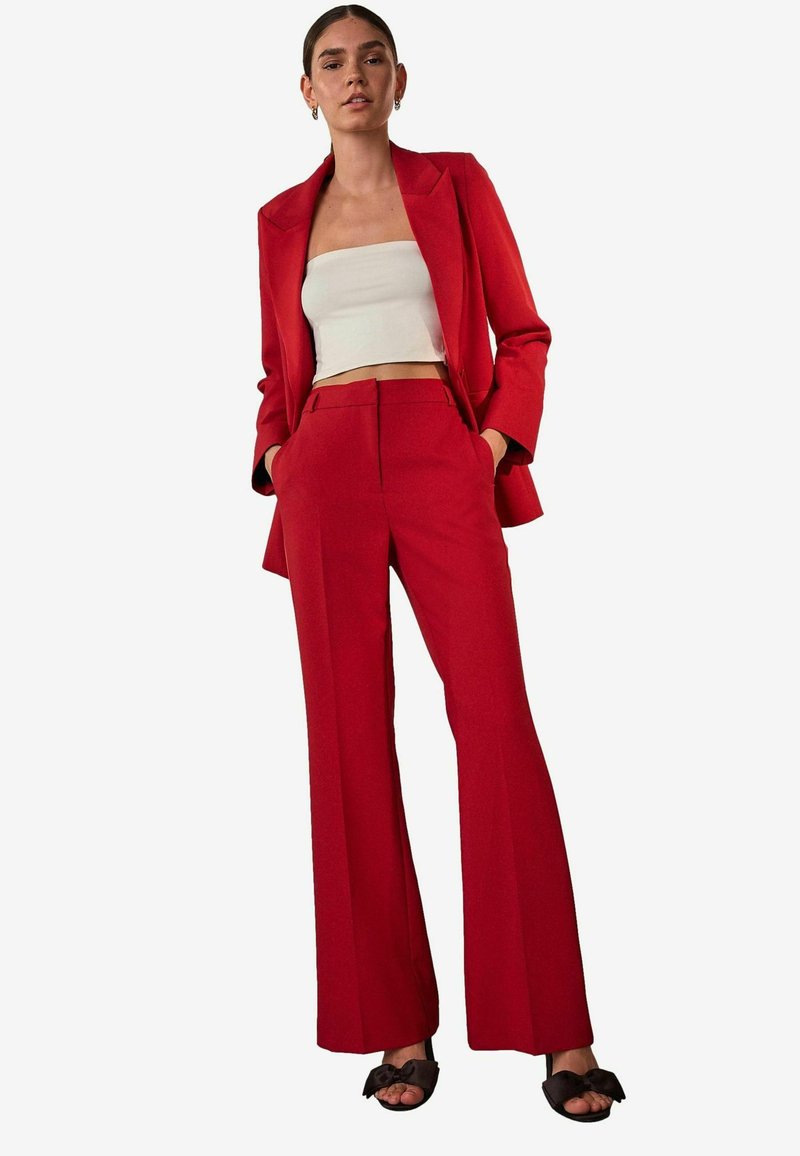 Punainen räätälöity bleiseri ja siihen sopivat liehuvat housut, yhdistettynä valkoiseen lyhytpaitaiseen toppiin. Sileä kangas ja jäsennelty malli, jossa sivutaskut.