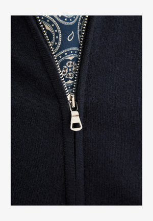 Granatowa kurtka typu zip z miękką teksturą, z metalowymi suwakami w kolorze srebrnym oraz wzorzystą niebieską podszewką widoczną przy otwarciu.