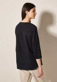 Blusa nera leggera con maniche a tre quarti, scollatura rotonda e sottili pieghe sul retro per una vestibilità rilassata.