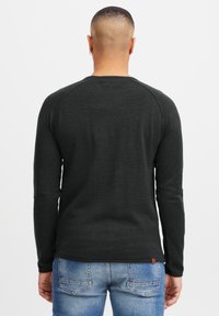 Svart langermet skjorte med teksturert stoff, med raglanerm og avrundet hem, kombinert med blå denimjeans.