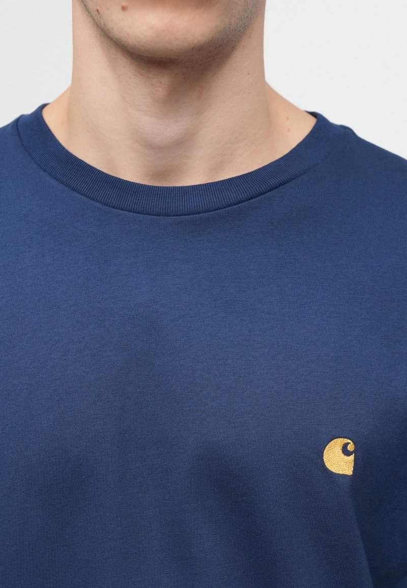 Mørkeblå bomulds t-shirt med rund halsudskæring og ribbet kant. Har et lille broderet logo i guld på venstre brystområde.