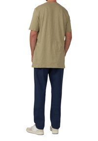 Oliwkowa bawełniana koszulka z krótkim rękawem w połączeniu z luźnymi granatowymi spodniami i białymi sneakersami, pokazana od tyłu.