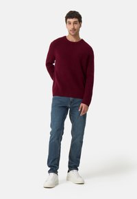 Burgundy ribbad tröja med rund halsringning, i kombination med ljusblå jeans och vita sneakers. Avslappnad, ledig passform.