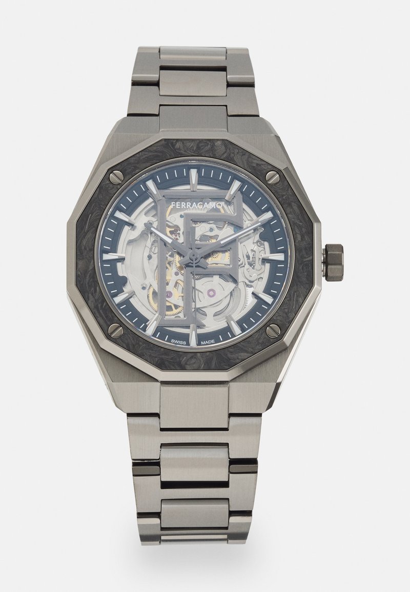 Stainless steel watch with an octagonal case, blue dial showcasing intricate machinery, and a brushed metal bracelet. Features Ferragamo branding.