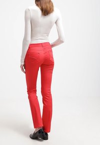 Pantalones rojos ajustados con una textura suave y corte Slim, que cuentan con dos bolsillos traseros con costuras decorativas, complementados por unos zapatos negros brillantes.