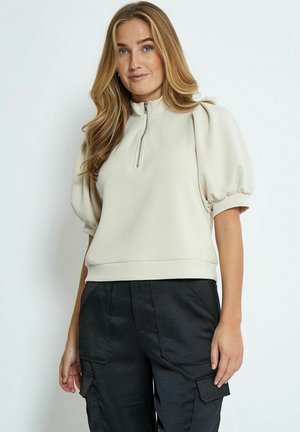 Felpa beige con zip, maniche corte a palloncino e finitura texture, abbinata a pantaloni cargo neri con tasche.