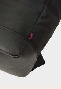 Zaino nero realizzato in tessuto resistente con una texture liscia. Presenta un piccolo etichetta con strisce rosse e blu e cuciture rinforzate.