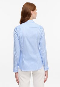 Blue and white striped long-sleeve shirt with a fitted design, button cuffs, and a curved hem, made from smooth fabric.