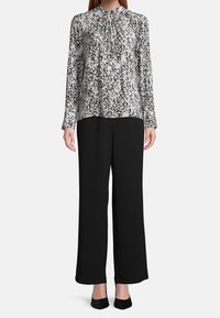 Black wide-leg pants paired with a long-sleeve blouse featuring a black and white swirl pattern, pleated neckline, and cuffed sleeves.