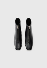 Pair of black leather ankle boots with front silver zippers and square toes on white background.