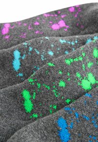 Chaussettes grises ornées de motifs éclaboussés colorés en rose, bleu et vert. Tissu texturé avec des lignes de couture visibles.