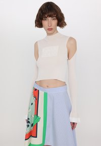 Csíkozott fehér crop top magas nyakkal és kivágott vállakkal, amelyet egy színes, mintás aszimmetrikus szoknyával viselnek, csíkokkal és virágos díszítésekkel.