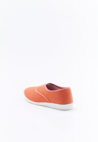Zapato slip-on de lona en color coral, con un exterior texturizado, entrada elástica y suela de goma blanca. El interior tiene un patrón a rayas.