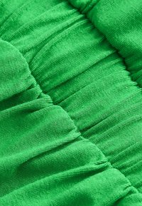 Tissu vert avec une texture froncée ; finition lisse et légèrement brillante. Présente des rayures horizontales de couture créant un motif ondulé.