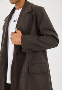 Brown wool blend overcoat with a single-breasted design, large lapels, two front pockets, and four-button accents on the cuff.