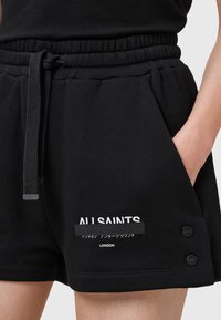 Juodos medvilnės šortai su elastinga juosmens juosta, raišteliu, šoninėmis kišenėmis ir spausdintu logotipu. Yra du juodi mygtukų akcentai ant apačios.