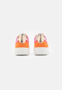 Baskets colorées avec des tiges en daim orange et rose, des accents dorés au talon et une semelle en caoutchouc blanc avec une texture antidérapante.