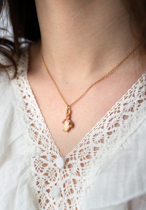 Gold chain necklace with a small rabbit pendant wearing a pink jacket, worn on a person in a white lace-trimmed blouse.