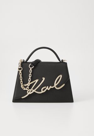 Bolso de mano de cuero negro con un diseño estructurado, correa de cadena dorada y un destacado detalle de la firma "Karl" en metal dorado.