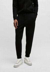 Svarta sweatpants i mjukt tyg, med elastisk midja och snörning, avslutade vid anklarna samt sidfickor, tillsammans med vita sneakers.