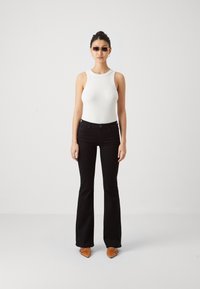 Jeans negri evazați cu talie ajustată, asortați cu un top din bumbac alb cu dungi, care are un guler texturat. Pantofi maro cu vârful ascuțit.