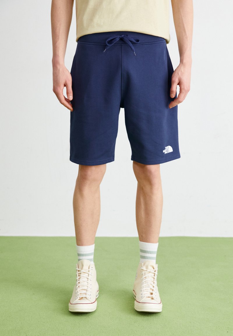 Shorts atletici blu navy in tessuto morbido, con vita elastica e cordino, e un logo bianco sul lato sinistro in basso.