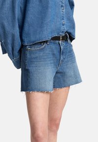 Denimshorts i ljusblått med fransade fållar och fem fickor. Bärs med en blå skjorta med knappar och ett svart bälte.