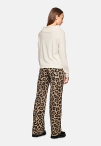 Cremfarbener Oversized-Pullover mit weit geschnittenem Kragen, kombiniert mit braunen weit geschnittenen Hose im Leopardenmuster. Texturiertem Stoff und schwarzen Akzenten bei der Fußbekleidung.