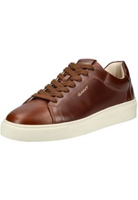 Zapatilla de cuero marrón con punta redonda, suela de goma blanca y cordones marrones. Presenta un logo sutil en el lateral y una textura suave.