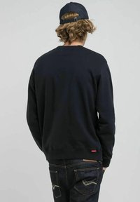 Felpa nera a girocollo in misto cotone, con polsini e orlo a costine, etichetta sul retro, indossata con jeans denim scuri.